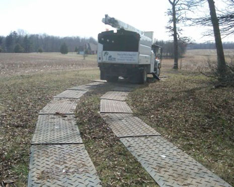 Large truck driving on ground protection mats laid out in two single tracks on a field between trees