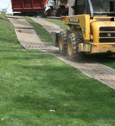Track mats on grass going up hill with a yellow digger driving on them